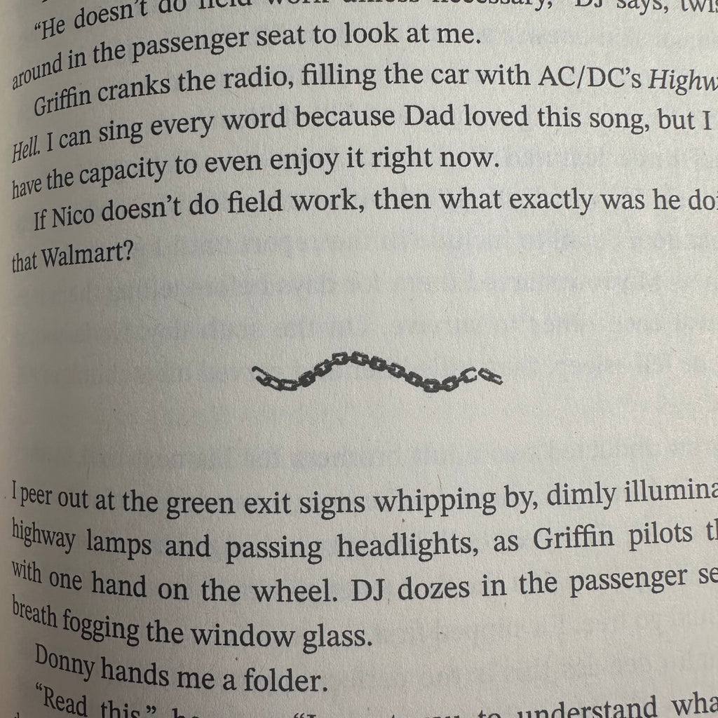 A close-up of printed text on a page, with a small black chain link or decorative chain centered on the page.