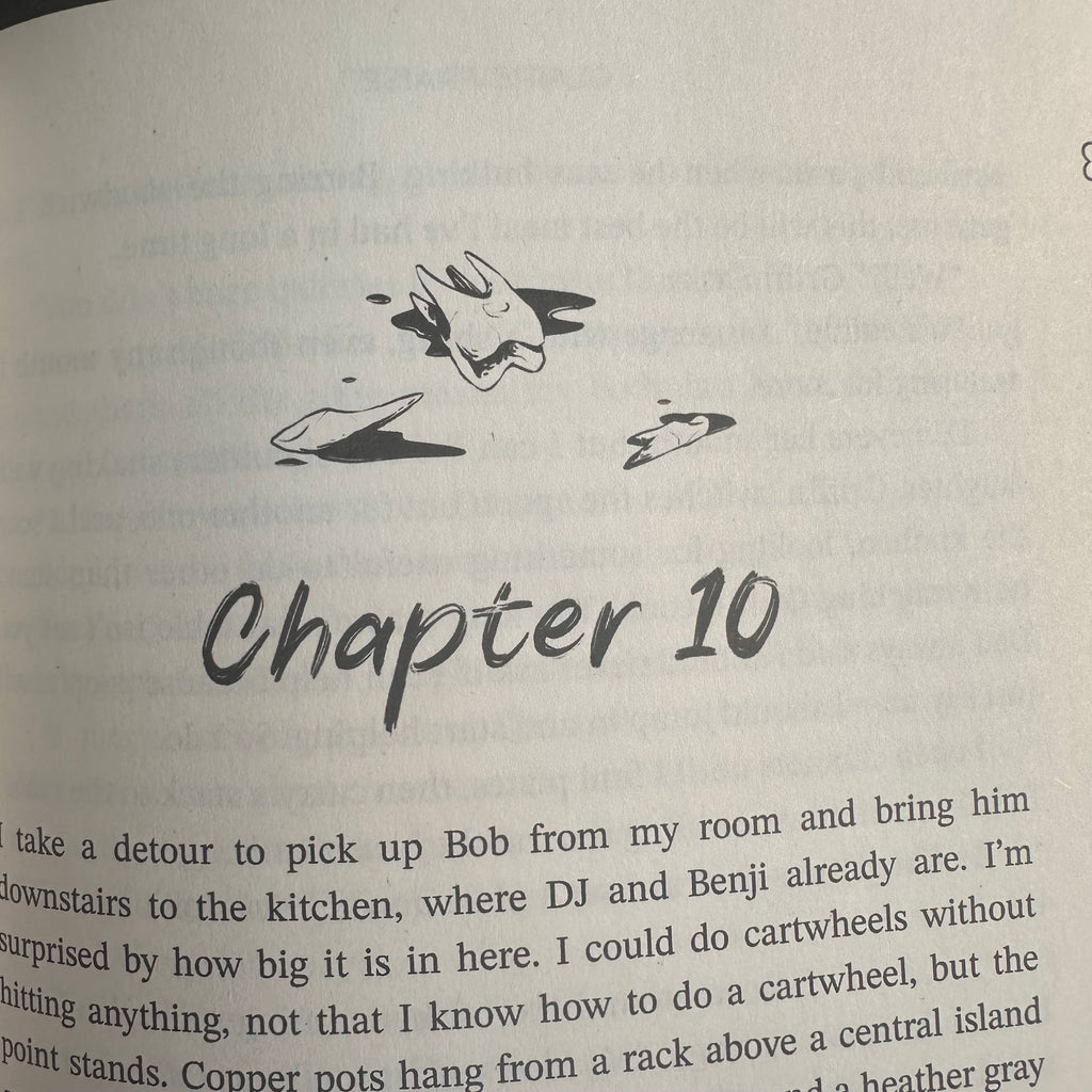 A close-up of a printed book page showing the handwritten title 'Chapter 10' in black ink, with a small black sketch and partial paragraphs of text on an off-white page.