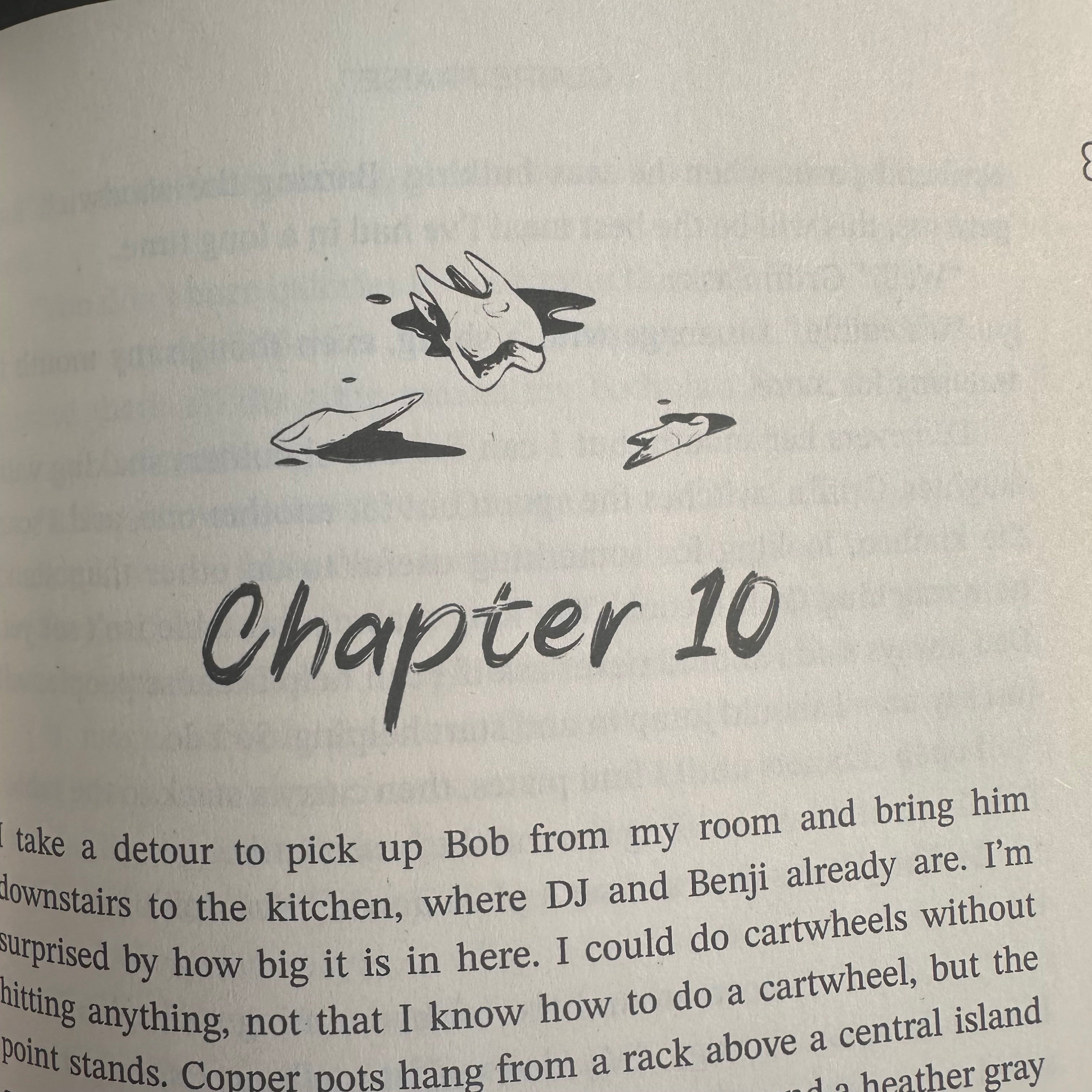A close-up of a printed book page showing the handwritten title 'Chapter 10' in black ink, with a small black sketch and partial paragraphs of text on an off-white page.